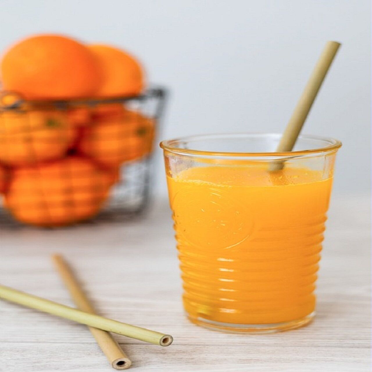 Un vaso de jugo de naranja con una pajita, un bol de naranjas y dos pajitas sobre una superficie de madera.