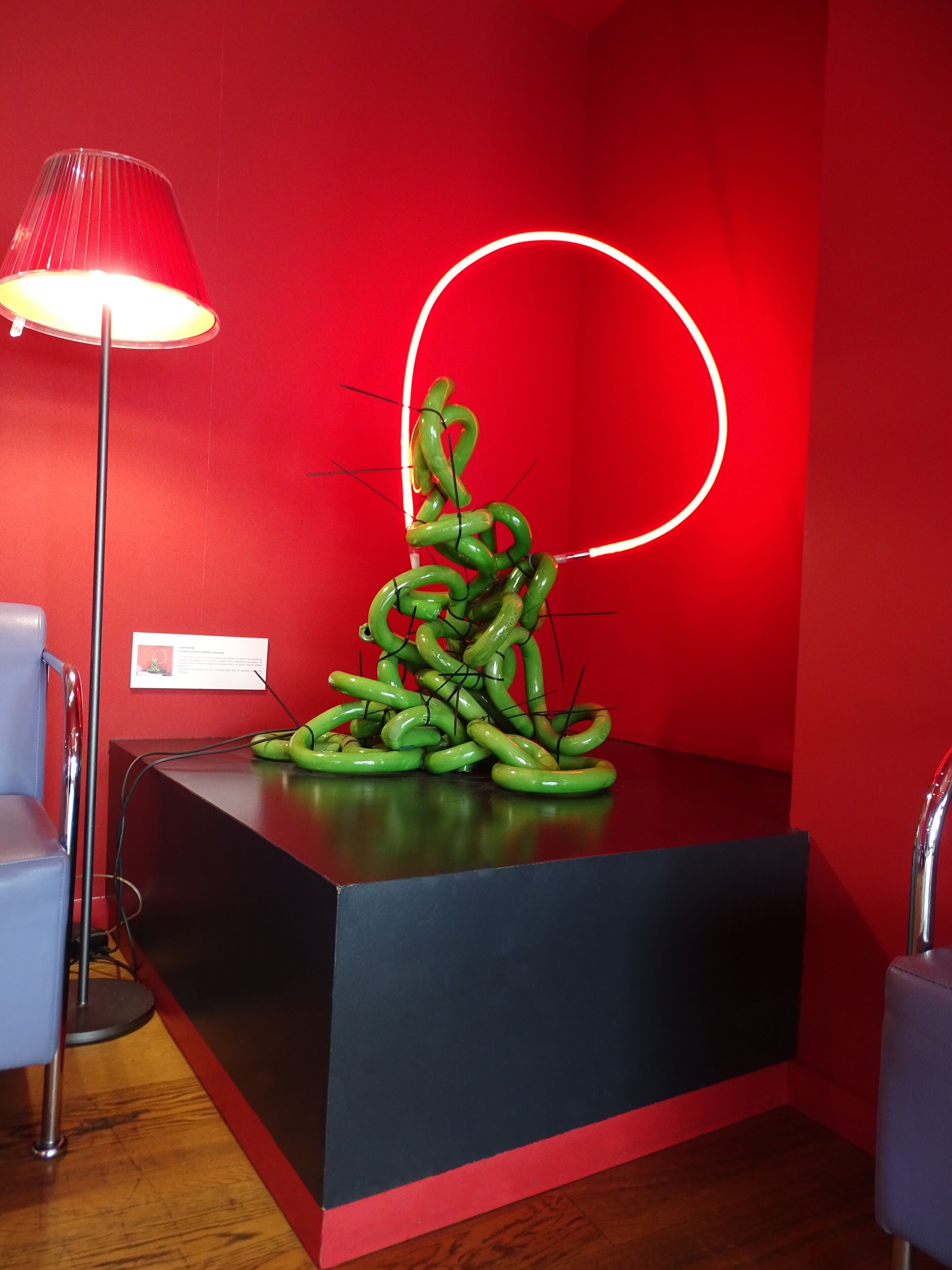 A reception desk with a green sculpture, a red wall, and a lamp.