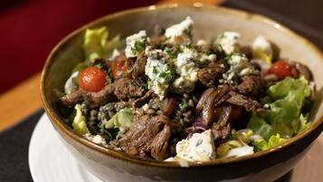 A bowl of salad with meat, tomatoes, and a creamy topping.