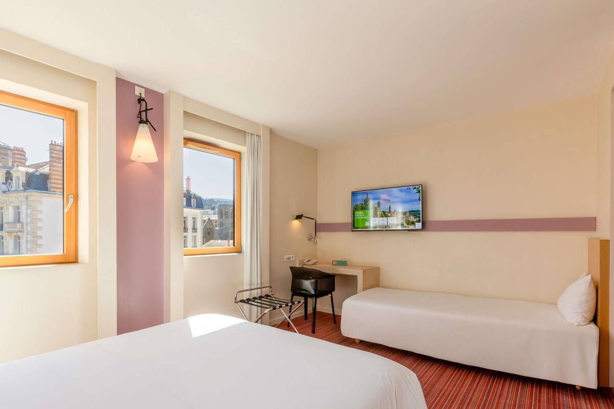 Une chambre d’hôtel avec deux lits, un bureau, une chaise, une télévision et une fenêtre donnant sur la ville.