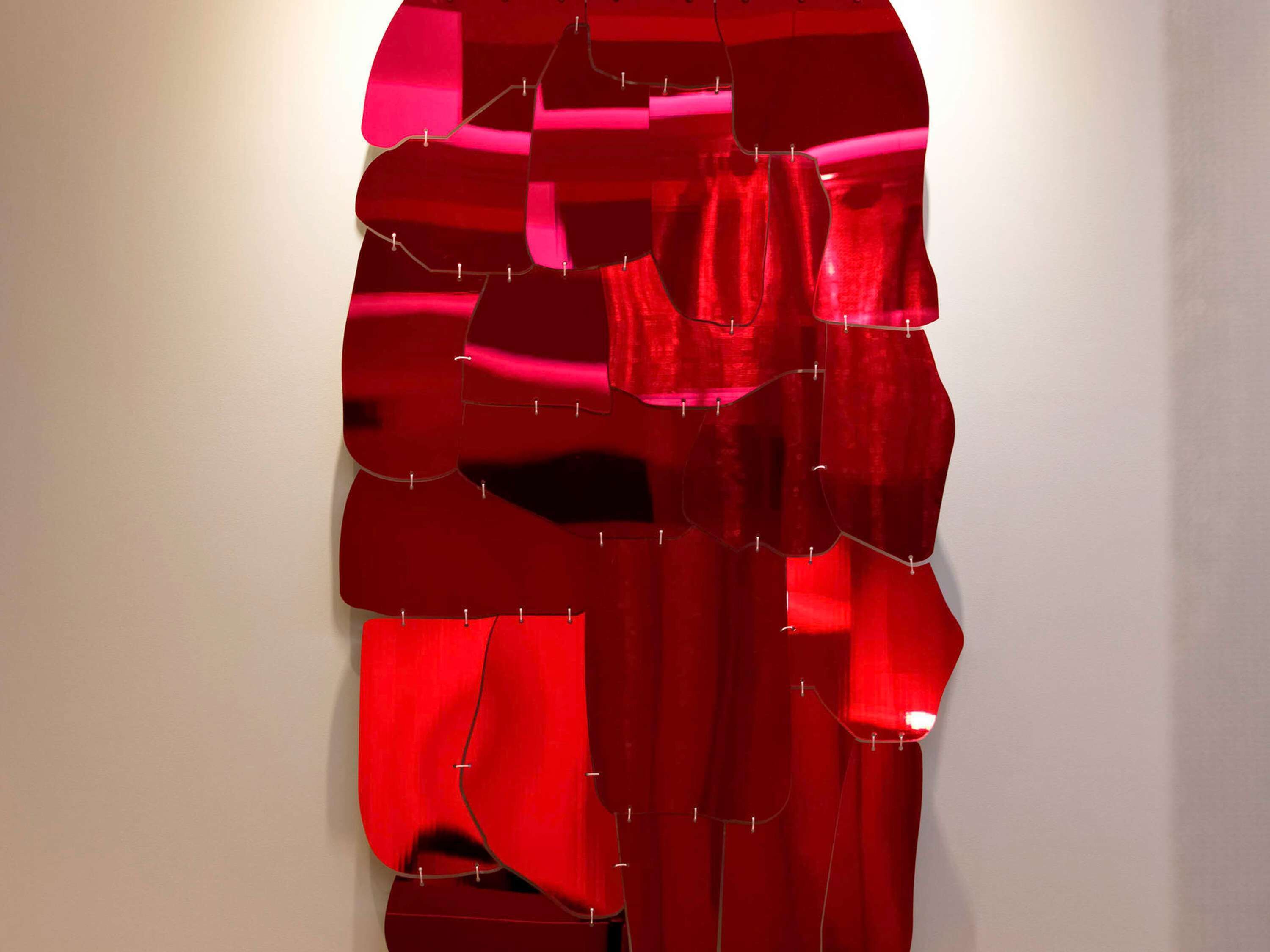 A red abstract art piece on a plain wall.