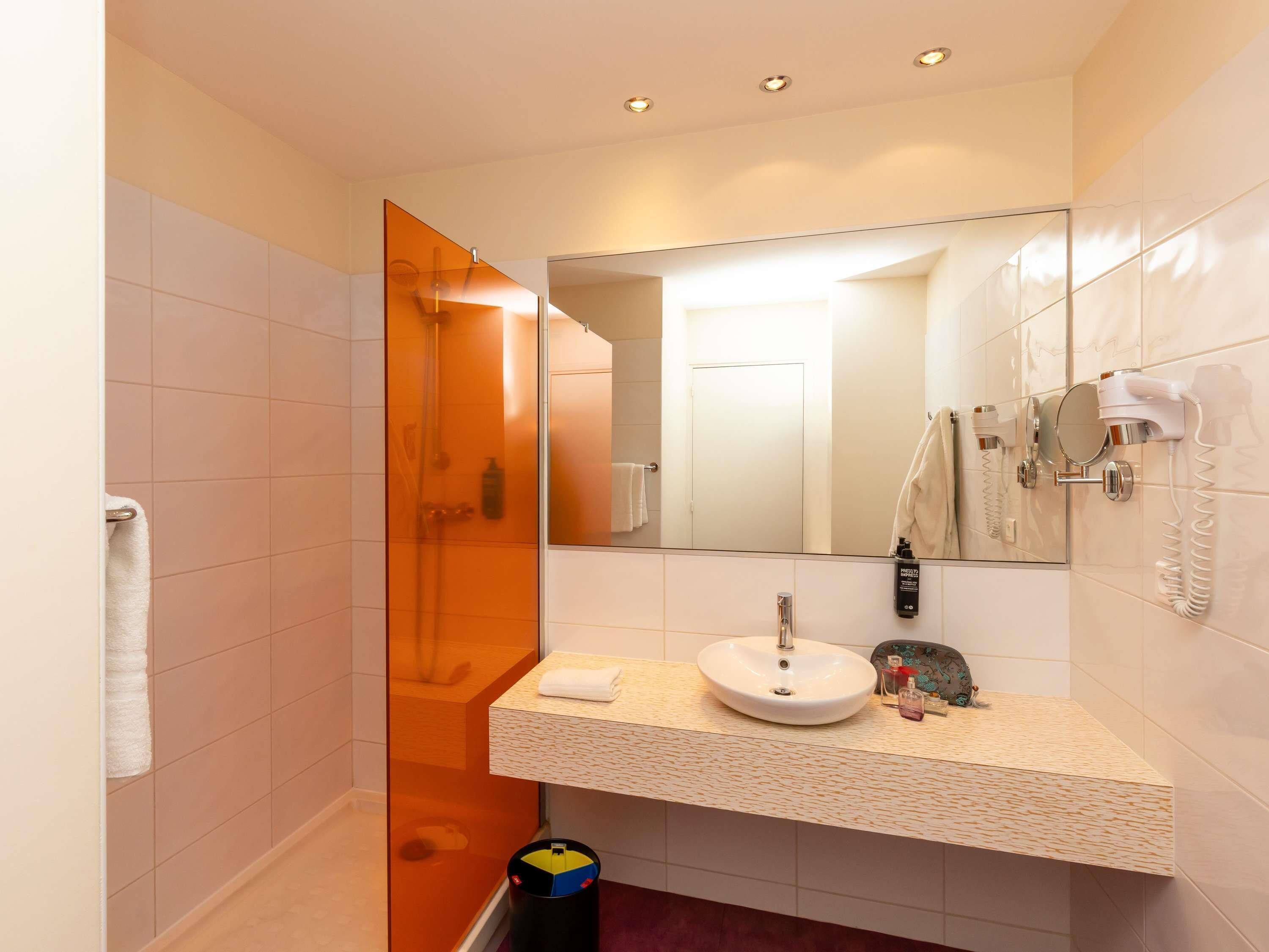 A modern bathroom with a glass shower enclosure, a sink with a mirror, and a hairdryer mounted on the wall.