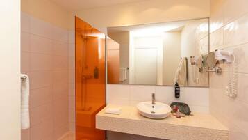 A modern bathroom with a glass shower enclosure, a sink with a mirror, and a hairdryer mounted on the wall.