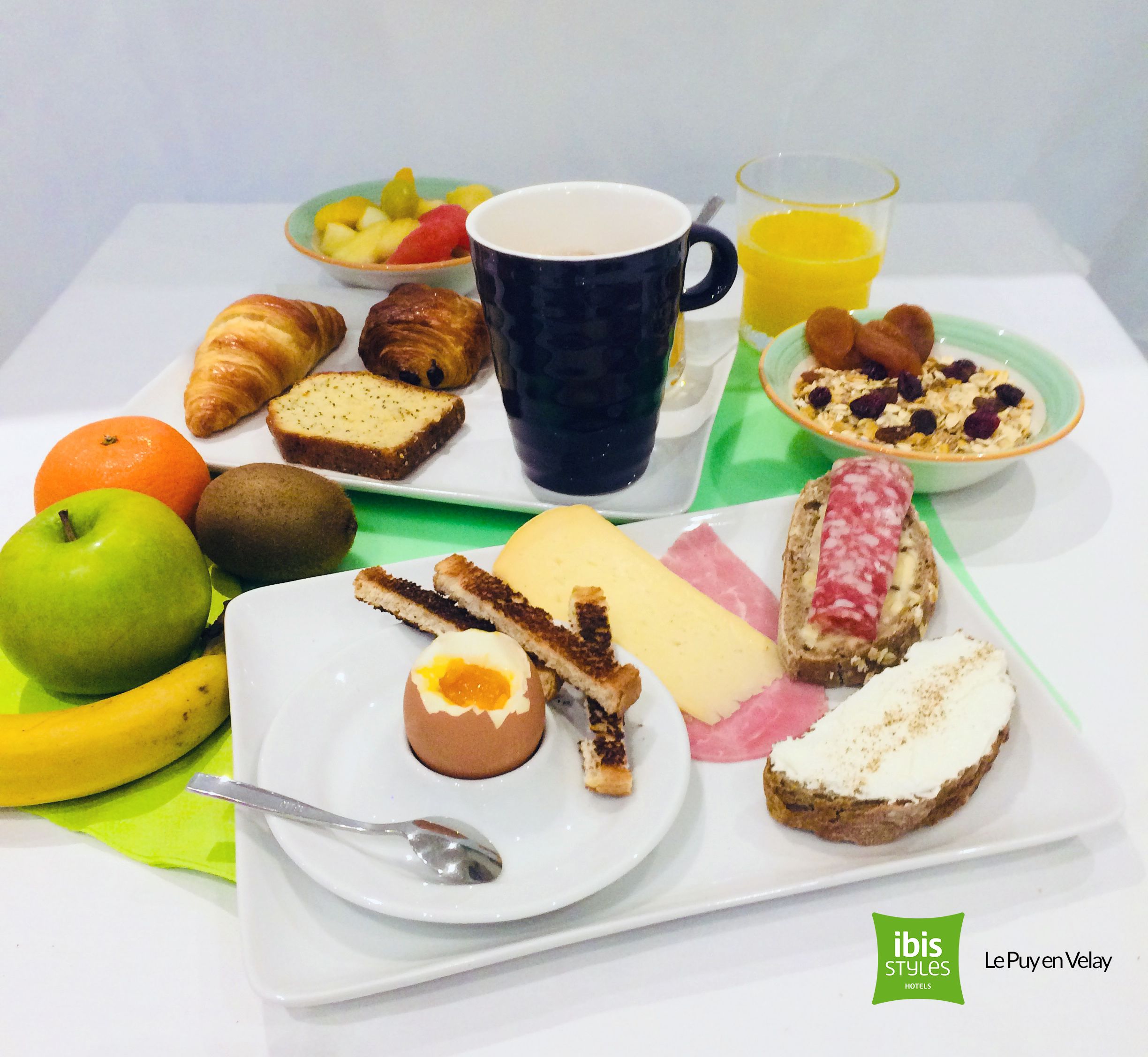 A breakfast tray with croissants, bread, cheese, ham, and a fruit bowl.