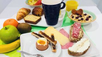 A breakfast tray with croissants, bread, cheese, ham, and a fruit bowl.