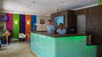 A reception desk with two staff members, a colorful wall, a television, and a green-lit counter.