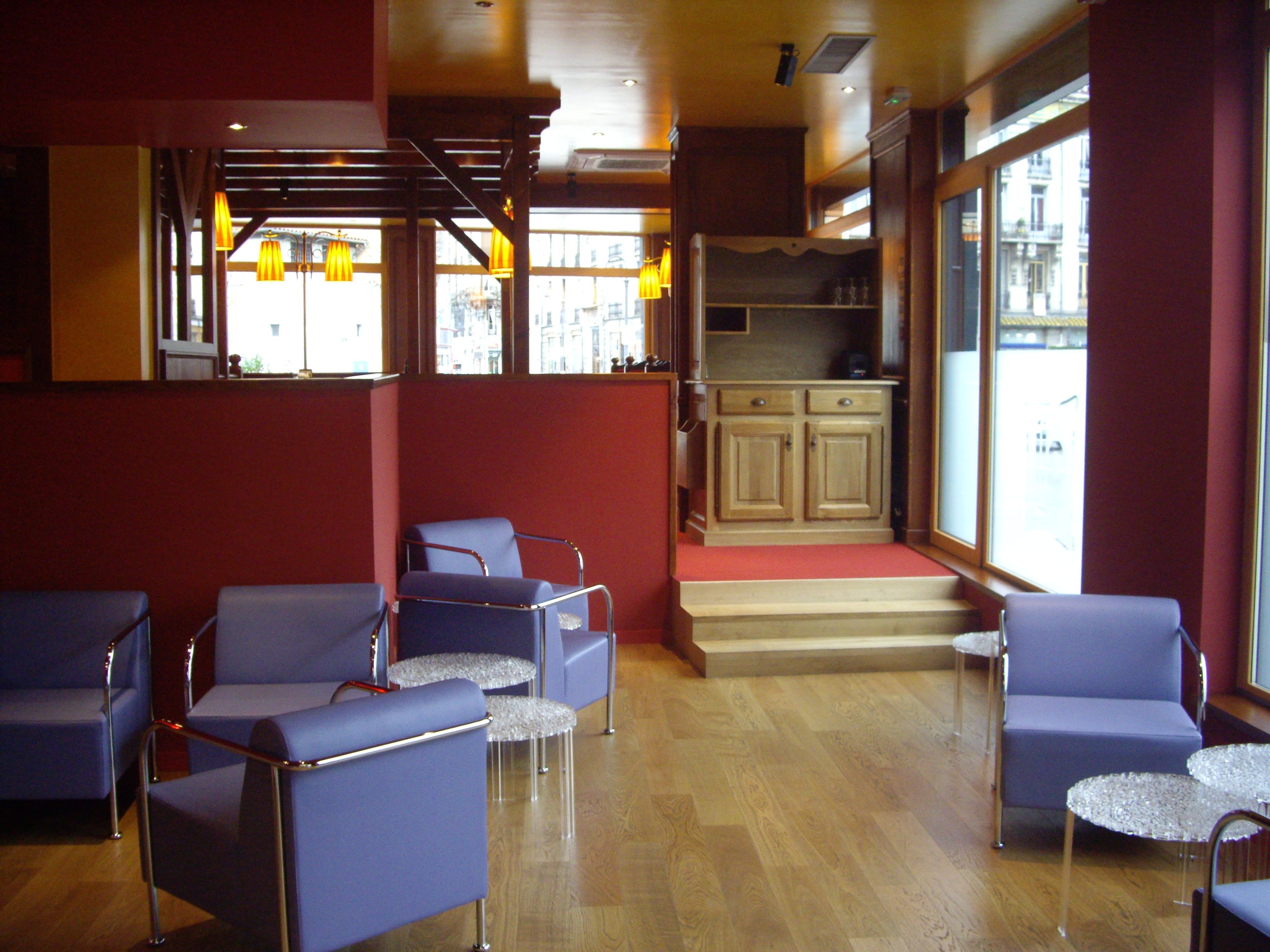 A hotel lobby with seating areas, a kitchen in the background, and large windows.