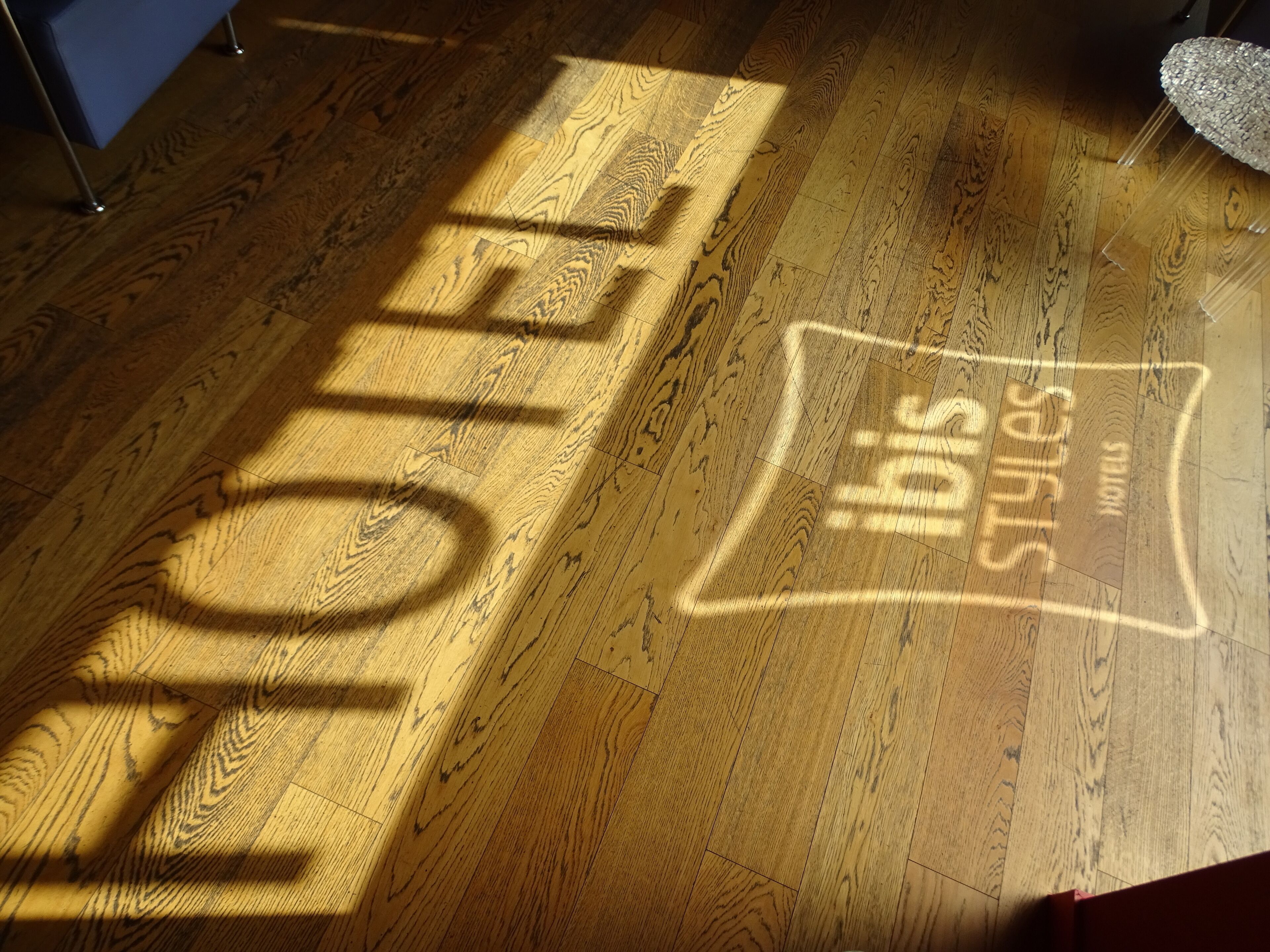 Un suelo de madera con la sombra de un letrero que dice "HOTEL" e "Ibis Styles Hotel".