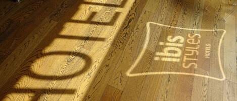 Un suelo de madera con la sombra de un letrero que dice "HOTEL" e "Ibis Styles Hotel".