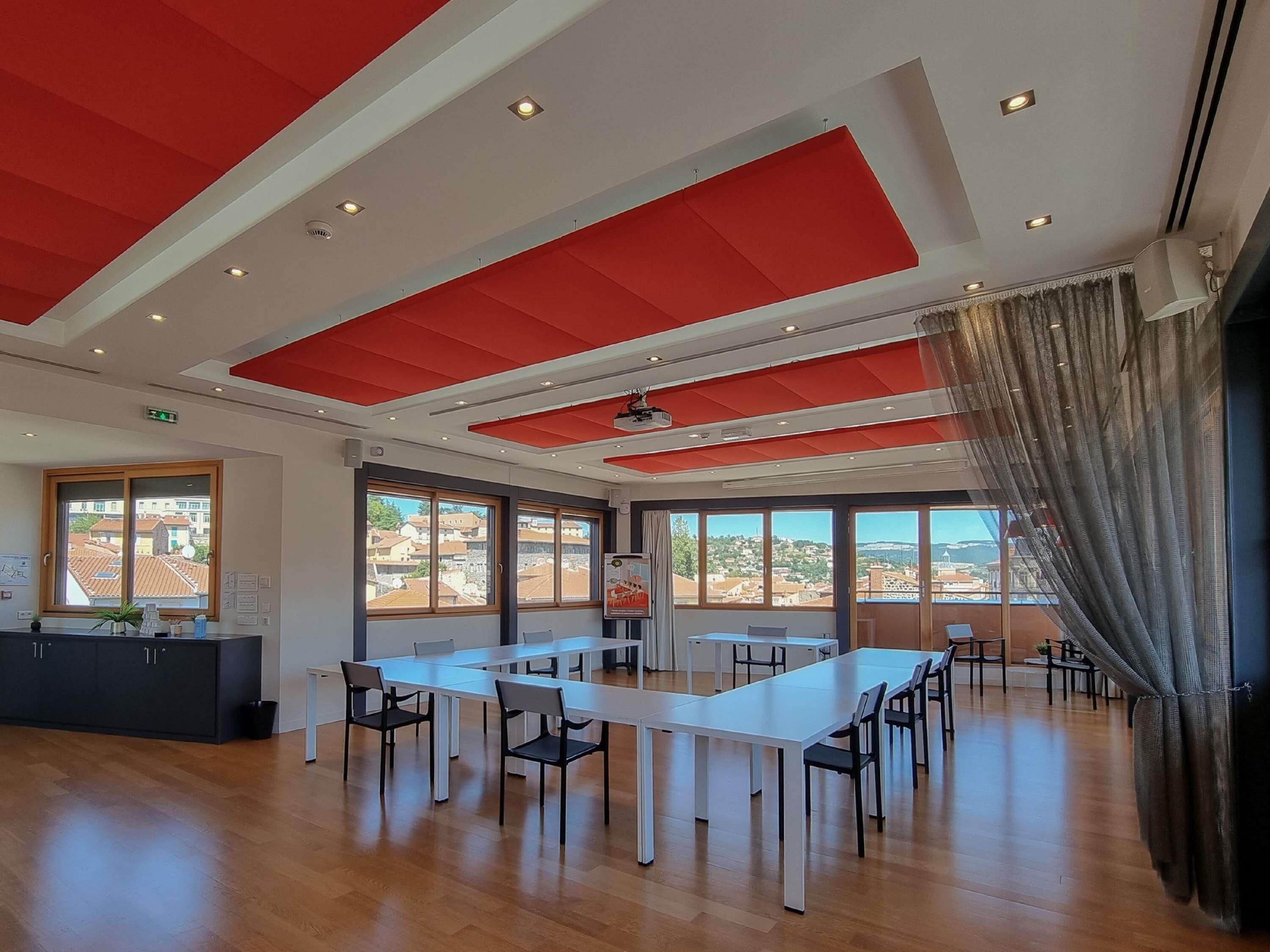 Une salle de conférence spacieuse, dotée d’une longue table et de chaises, de grandes fenêtres offrant une vue dégagée et d’un plafond rouge.