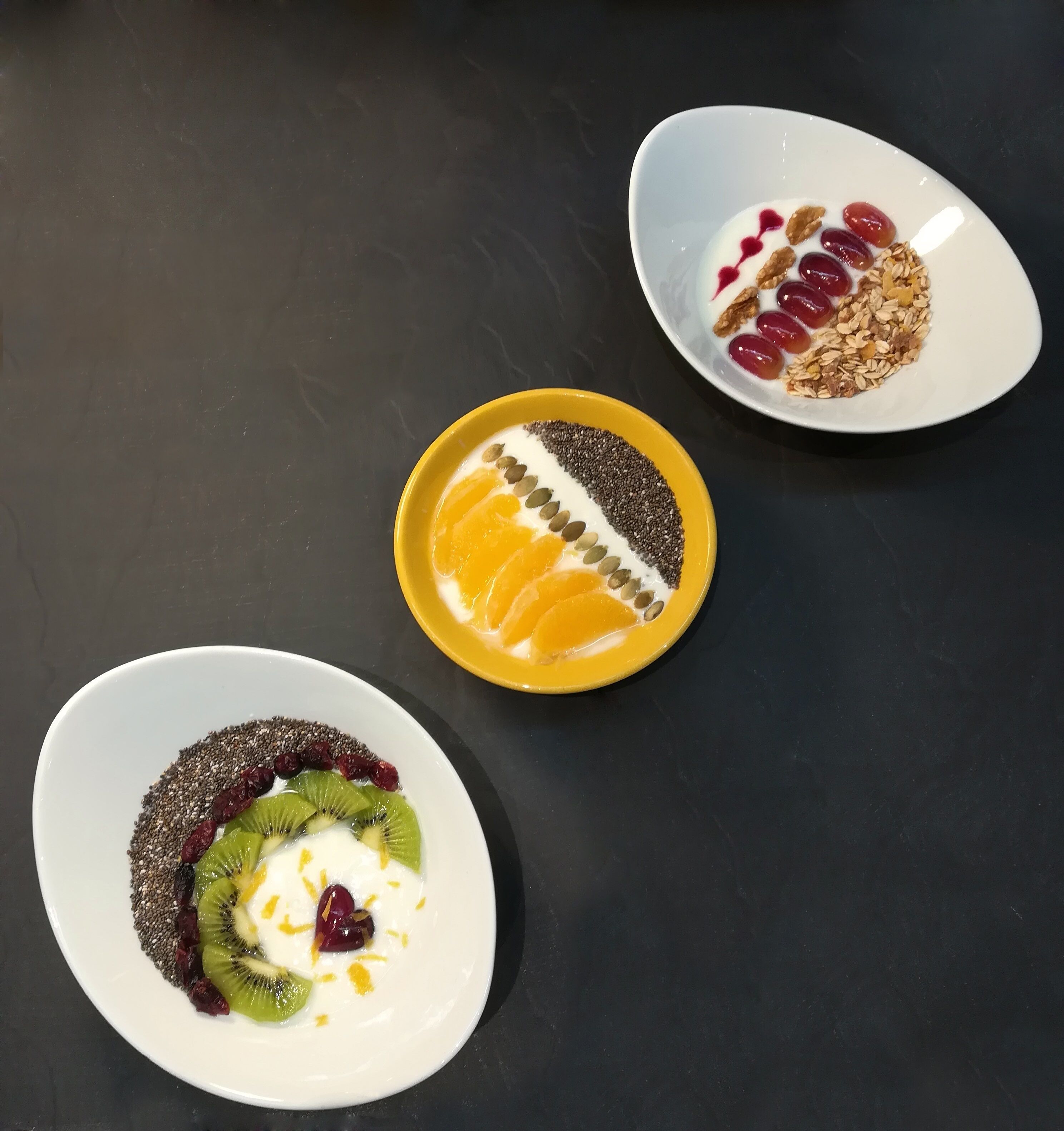 Three bowls of food with different toppings on a dark surface.