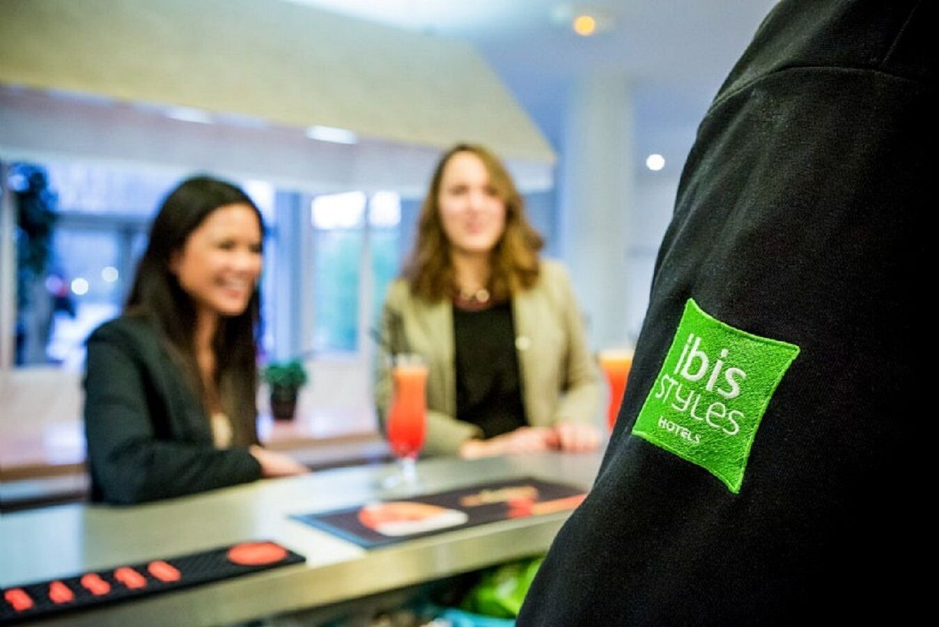 A person wearing a black jacket with a green label that reads "ibis Styles Hotels".