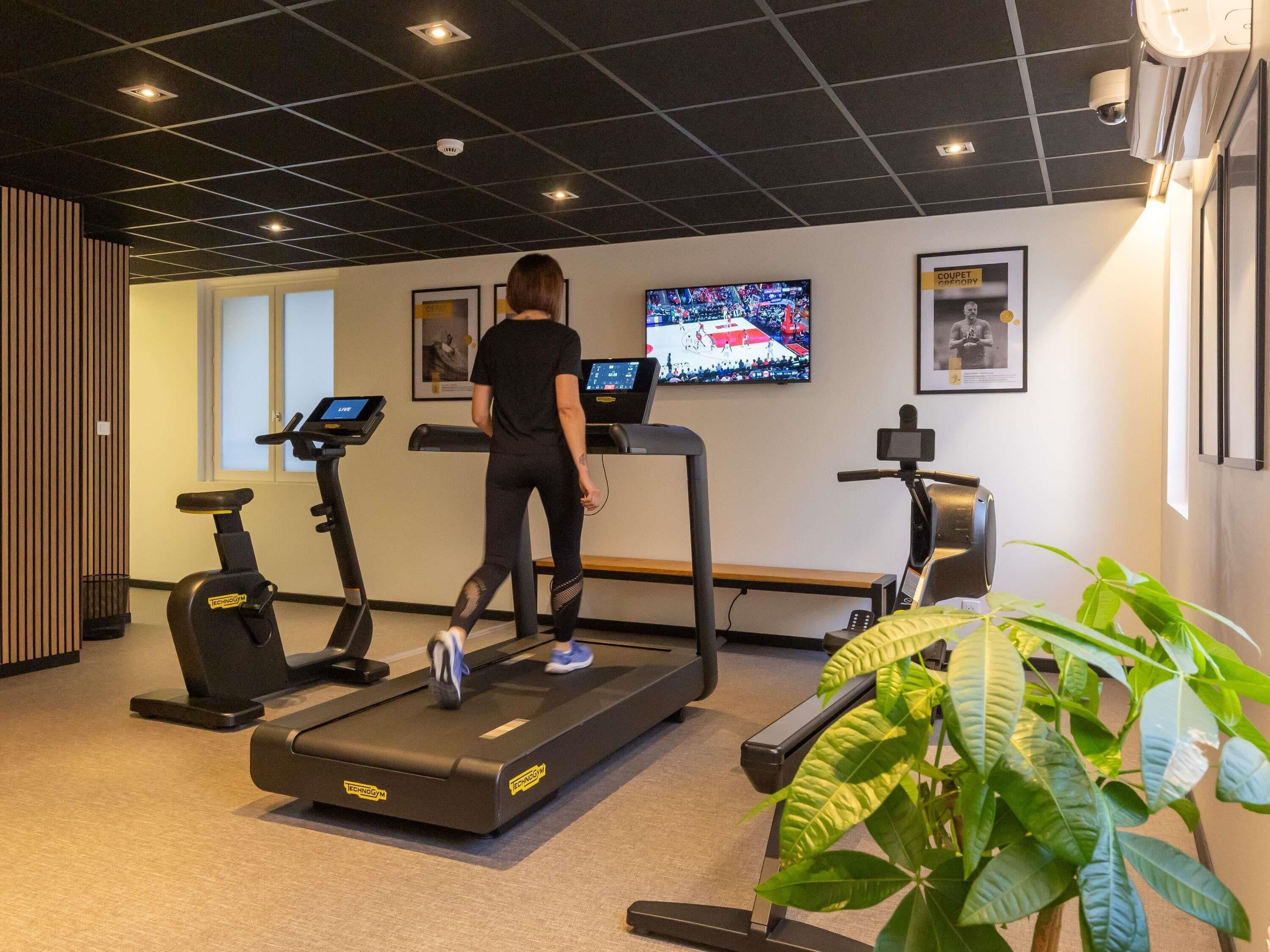 Ein Fitnessraum mit Laufbändern, Ergometer und einem Fernseher, der ein Sportereignis zeigt.