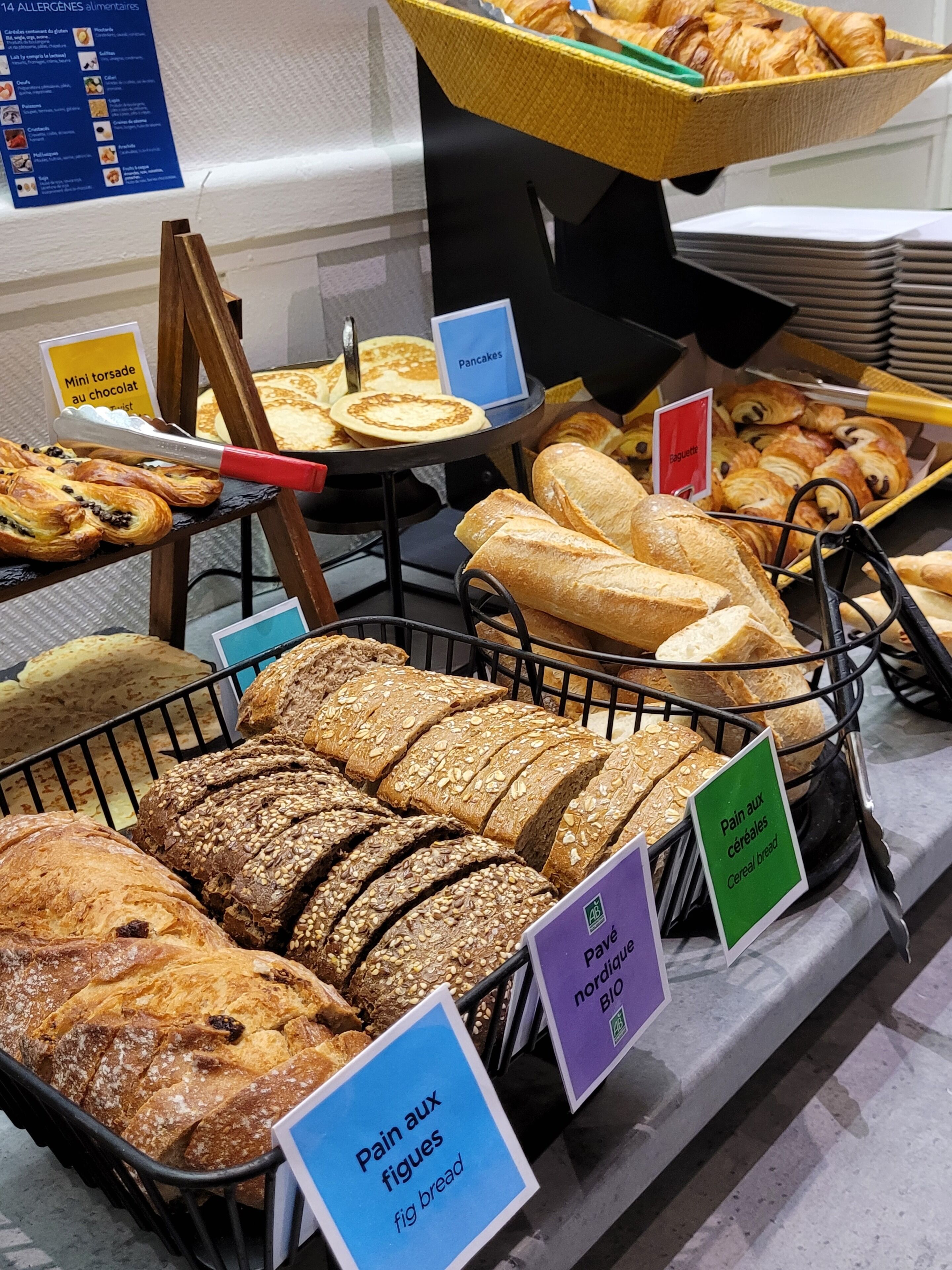 A bakery display with various types of bread and pastries, including mini chocolate tarts and pancakes.