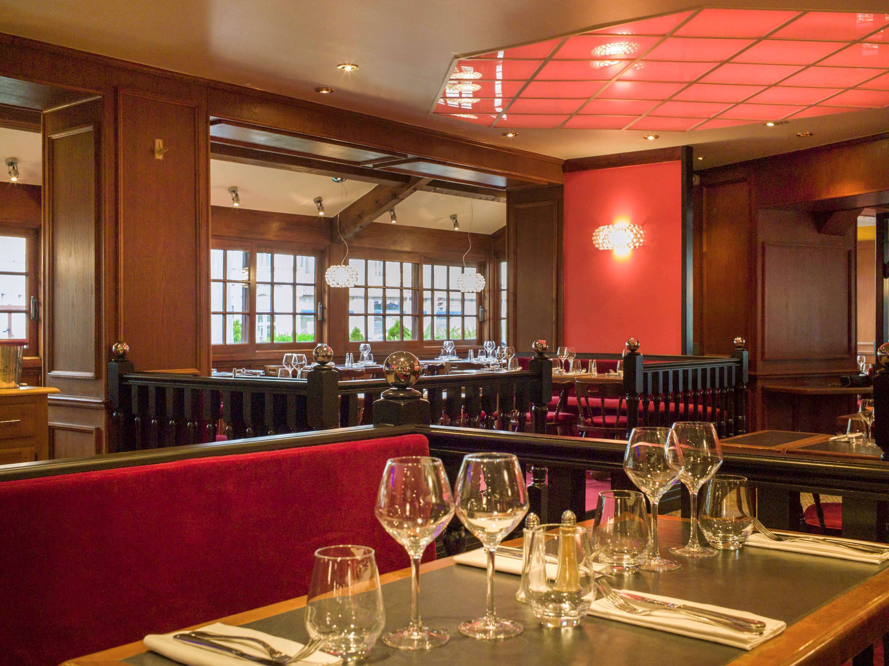 Ein Restaurant Innenraum mit Holzwänden, rot gepolsterten Sitzecken und einer roten Akzentwand. Die Tische sind mit Weingläsern und Besteck gedeckt.