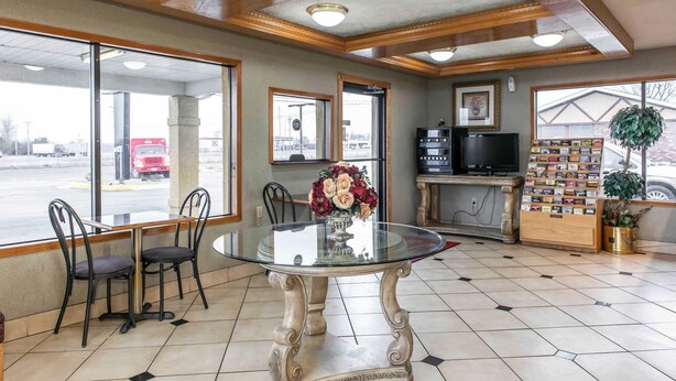 A restaurant interior with a glass table, two chairs, a vase of flowers, a television, a menu board, and a view of the outside. - Econo Lodge Seymour (Seymour)