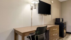 A hotel room with a wooden desk, a black chair, a flat-screen TV mounted on the wall, a small black refrigerator, and a wall-mounted lamp. - Econo Lodge Seymour (Seymour)