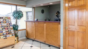 A reception area with a wooden counter, a clock, a plant, and a display of postcards. - Econo Lodge Seymour (Seymour)