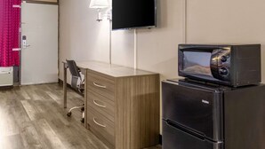 A compact hotel room with a wooden desk, a black refrigerator, a microwave, a flat-screen TV, and a lamp. - Econo Lodge Seymour (Seymour)