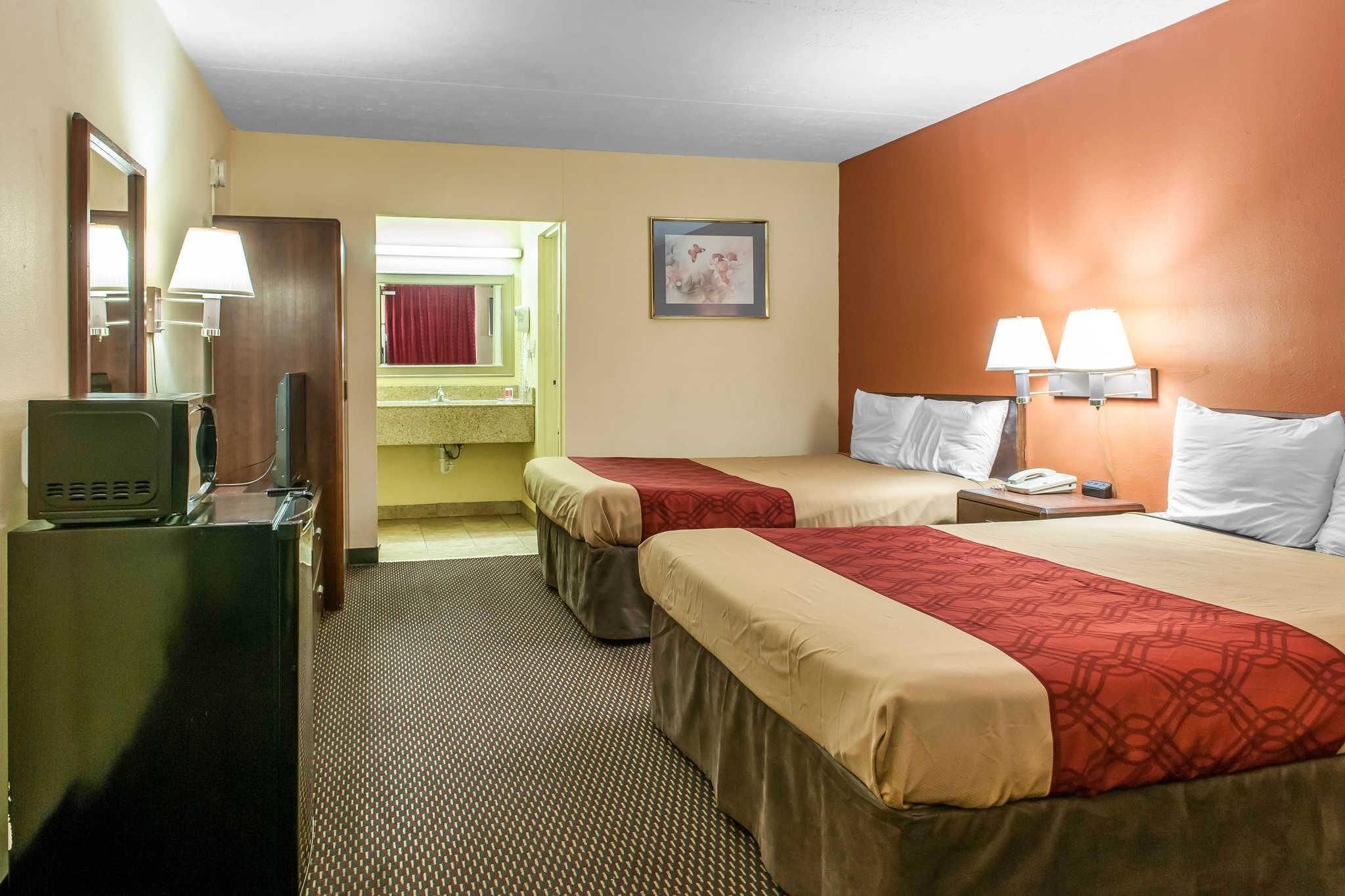 A hotel room with two beds, a desk with a computer, a mirror, and a bathroom visible through an open door.