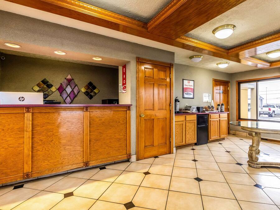 A hotel lobby with wooden reception desks, a glass-top table, and a view of the parking area through the door.