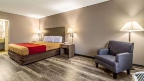 A hotel room with a bed, two bedside lamps, a chair, and a nightstand. - Econo Lodge Seymour (Seymour)