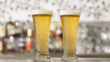 Two tall glasses of beer on a bar counter with a blurred background of bottles.