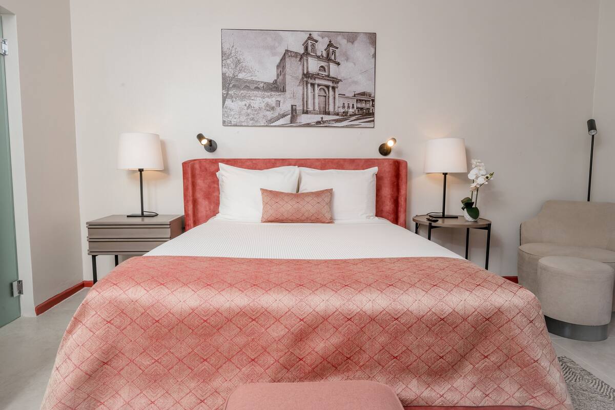 A neatly arranged hotel room with a large bed, two bedside tables with lamps, a small side table with a plant, and a chair.