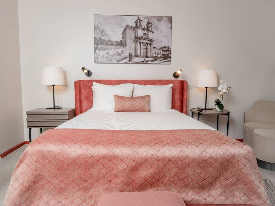A neatly arranged hotel room with a large bed, two bedside tables with lamps, a small side table with a plant, and a chair.