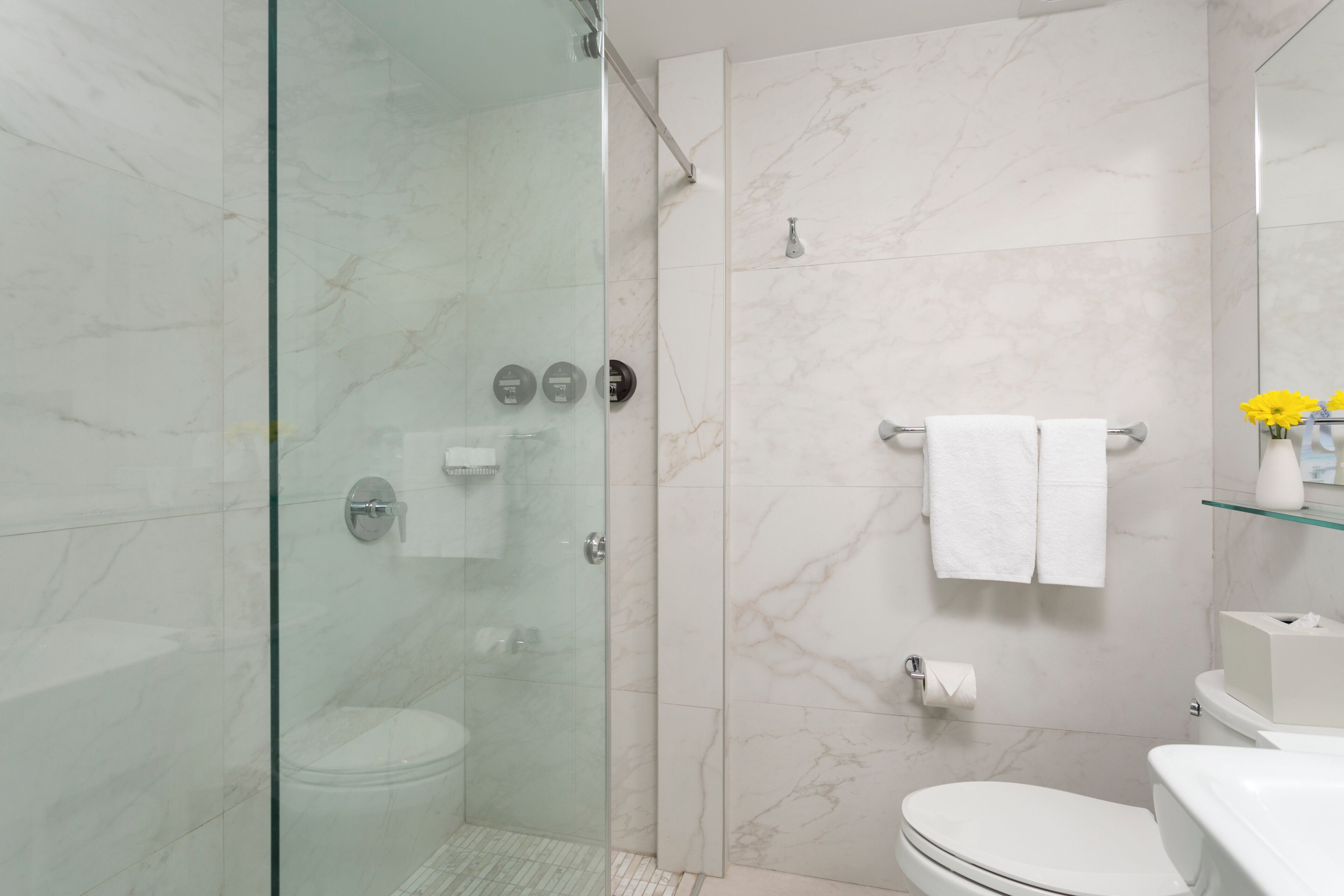 Un baño moderno con ducha de vidrio, inodoro y repisa de vidrio con artículos de aseo.
