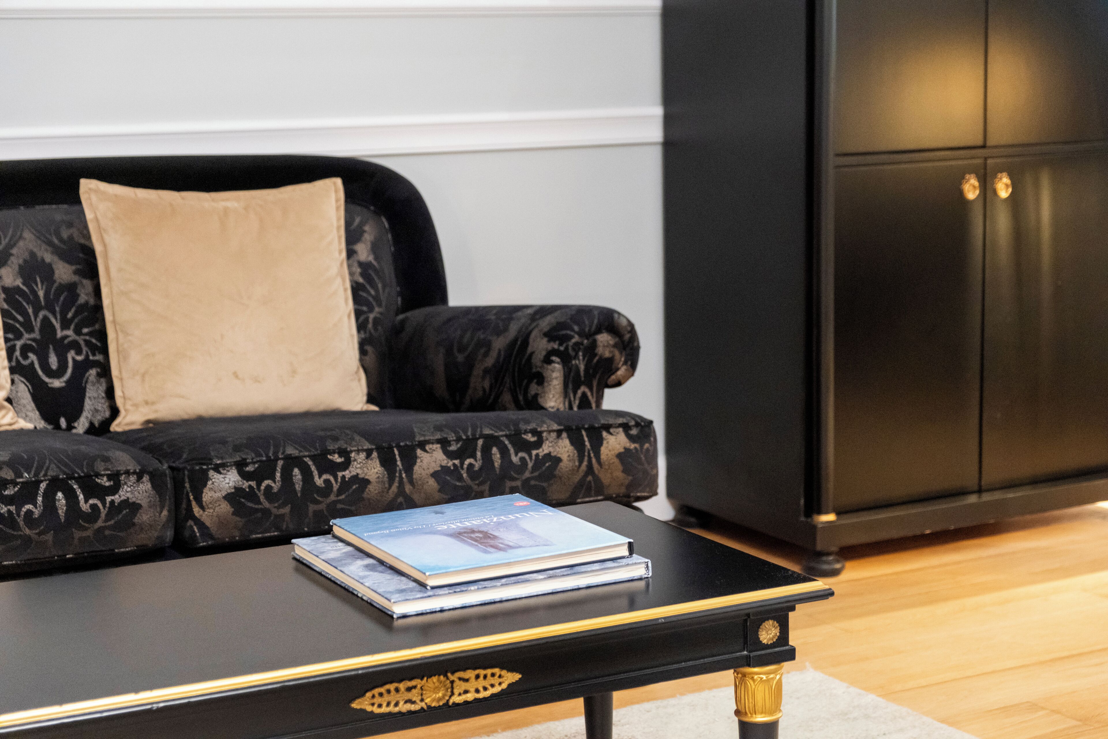 A black sofa with a patterned fabric and a beige cushion, a black coffee table with gold accents, and a black cabinet with gold handles.