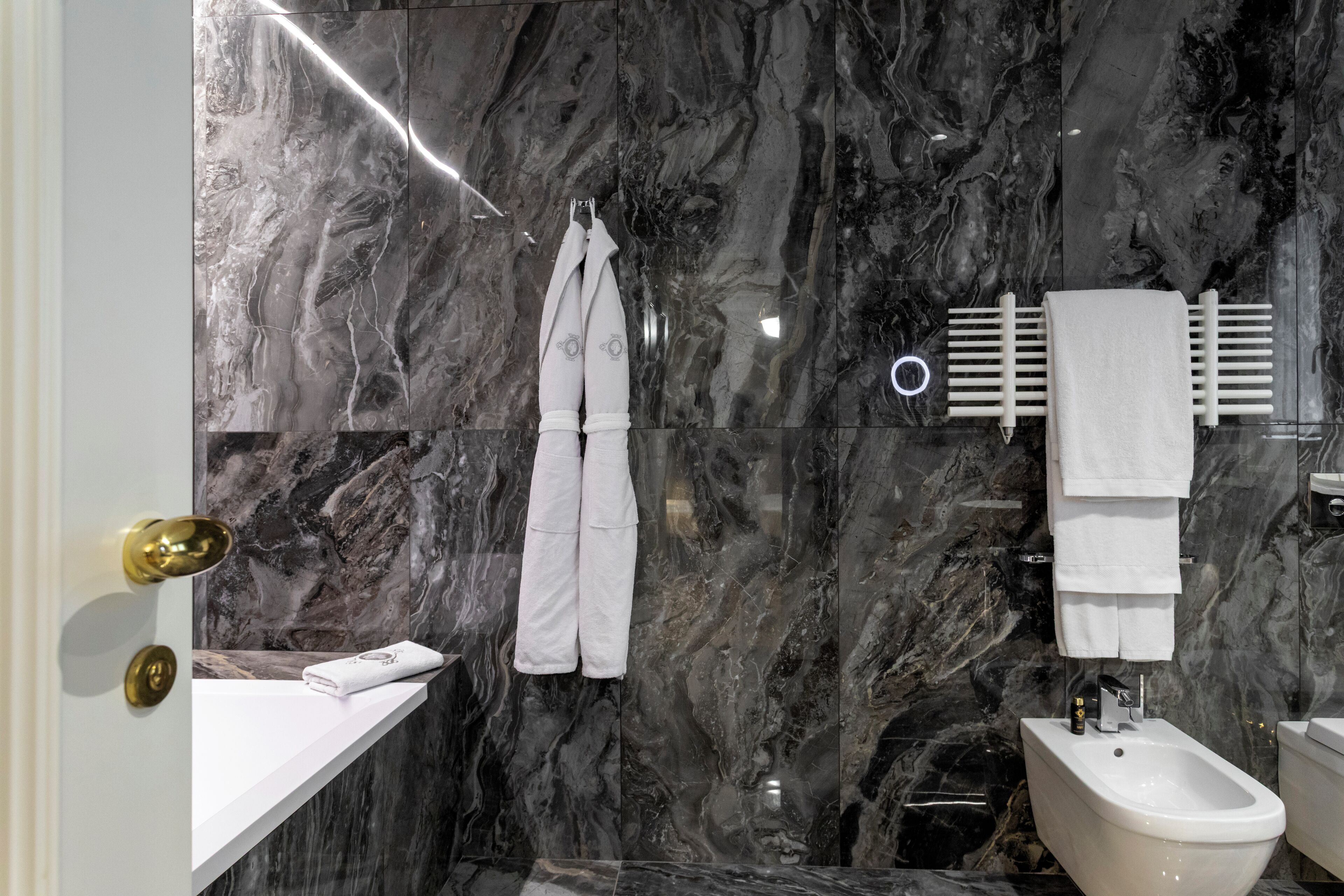 A modern bathroom with marble walls, a white sink, a bidet, and a towel rack.