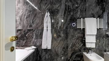 A modern bathroom with marble walls, a white sink, a bidet, and a towel rack.