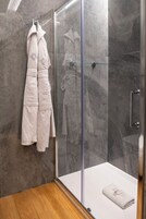 A modern bathroom with a glass shower enclosure, marble walls, and a wooden floor.
