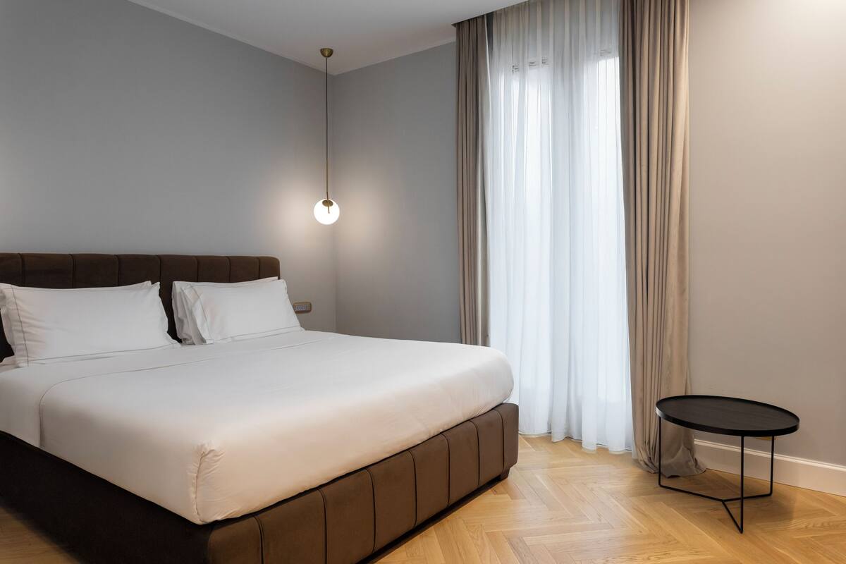 A bedroom with a large bed, a small round table, and a hanging light fixture.