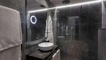 A modern bathroom with a large mirror, a round light fixture, a glass-enclosed shower, and a black countertop with a white sink.