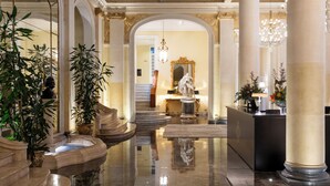 Un lobby imponente con suelos de mármol, amplias columnas, una gran escalera y una recepción.