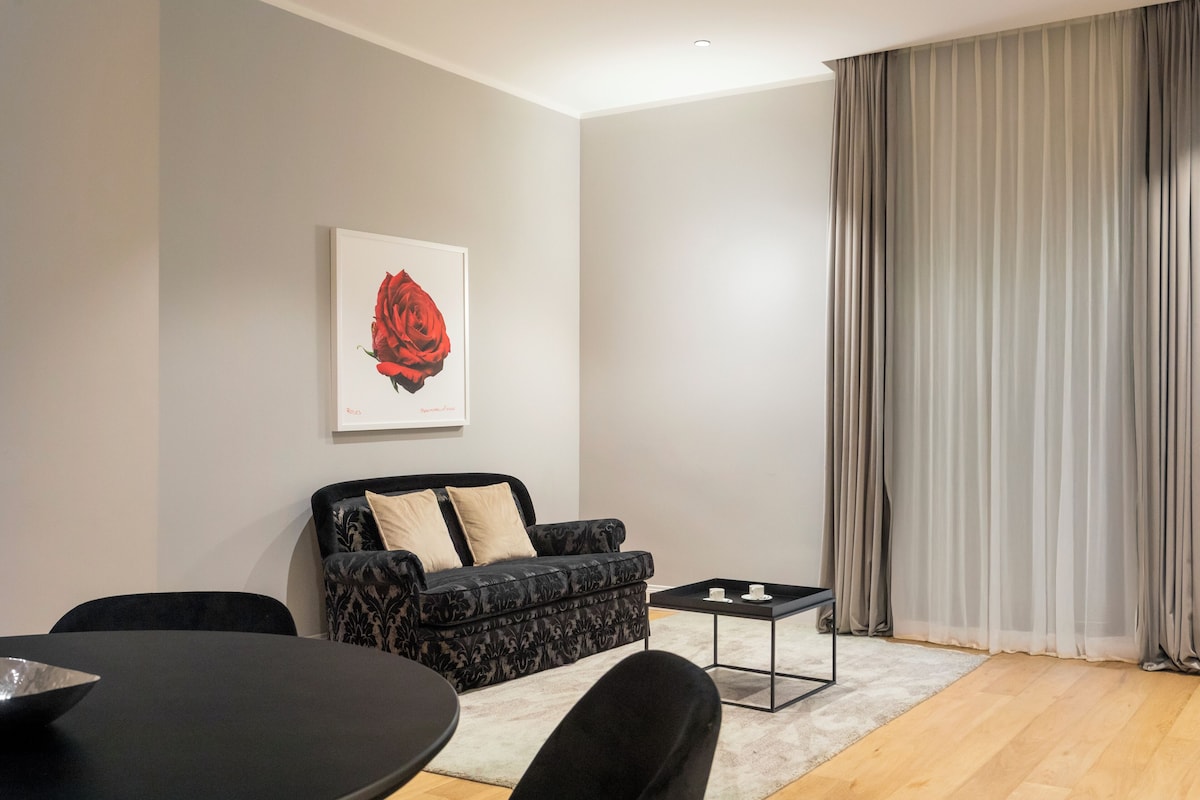 A modern living room with a black sofa, a small black coffee table, and a dining table with a bowl.