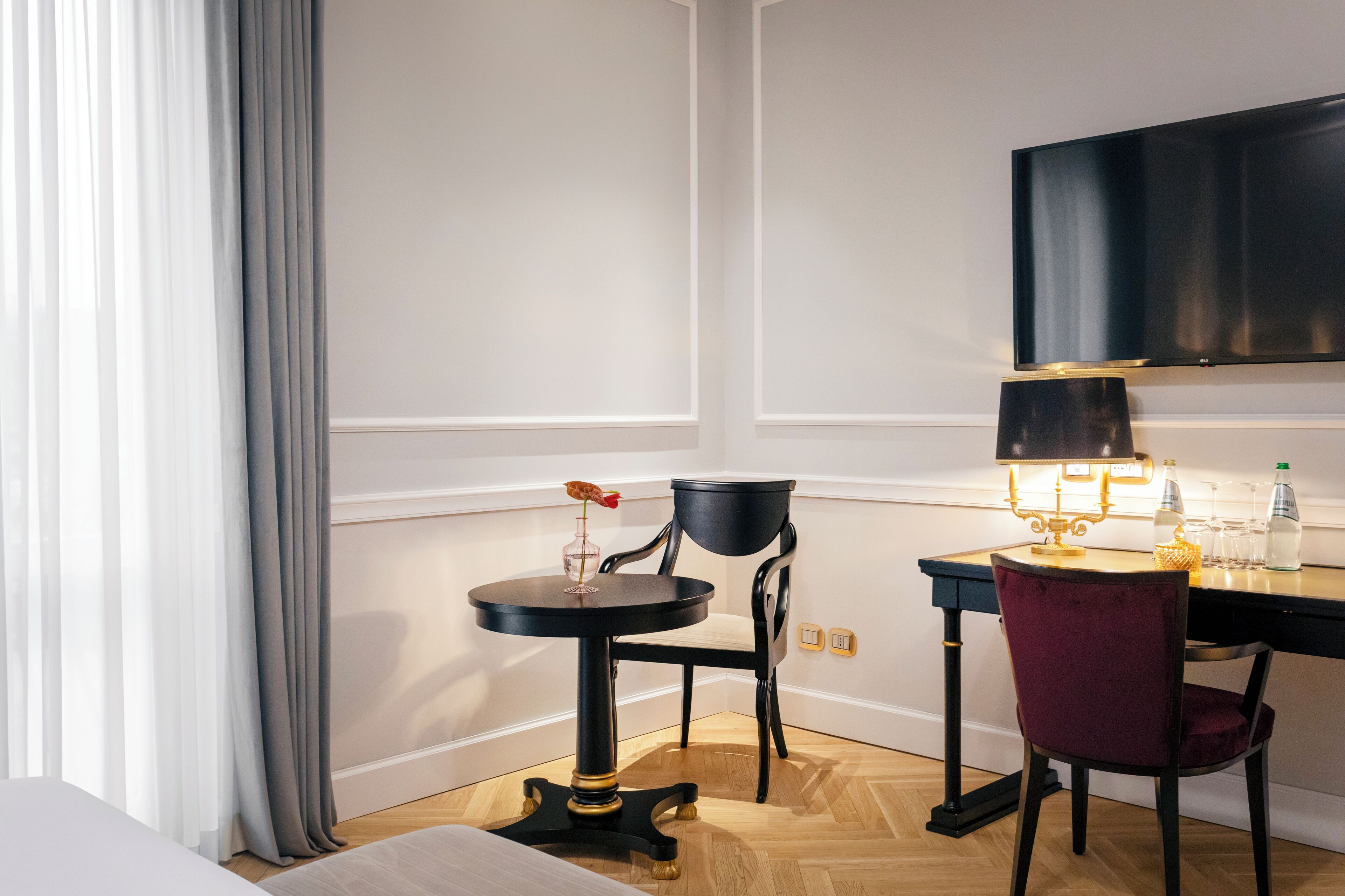 Une chambre d’hôtel avec un lit, une table ronde avec une lampe, une chaise et un téléviseur fixé au mur.