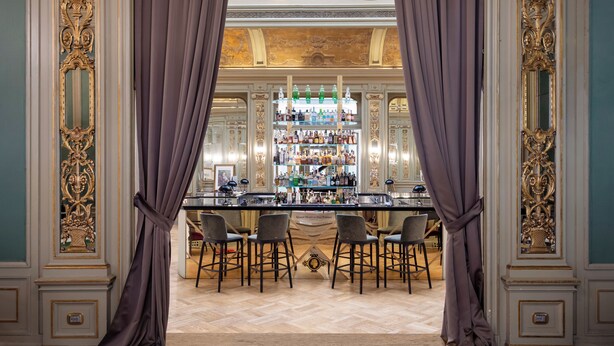 A bar area with a bar counter, multiple stools, and a well-stocked shelf with bottles. - Grand Hotel et Des Palmes (Palermo)