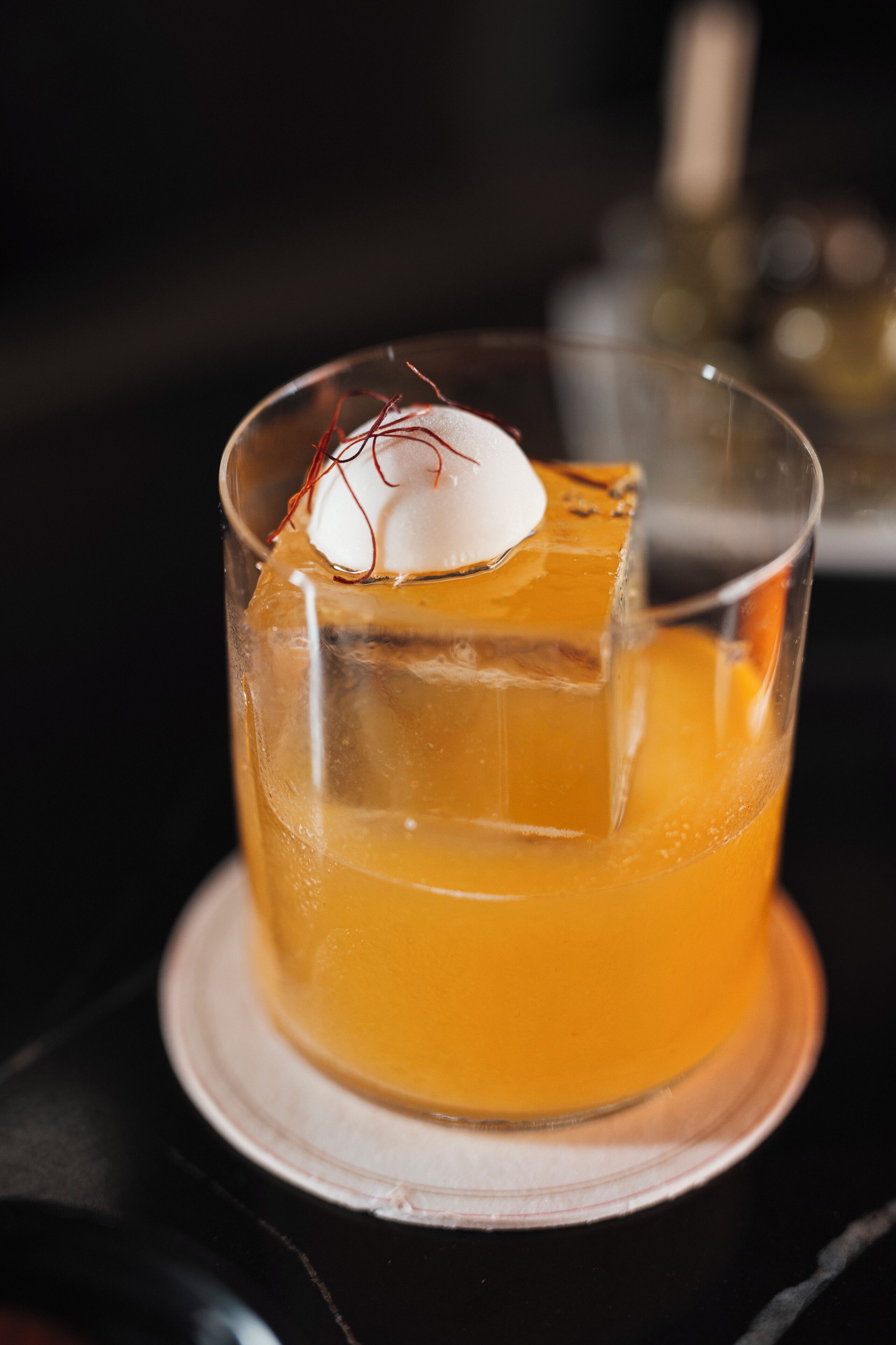 A clear glass with a yellow beverage, ice, and a decorative element on a coaster.