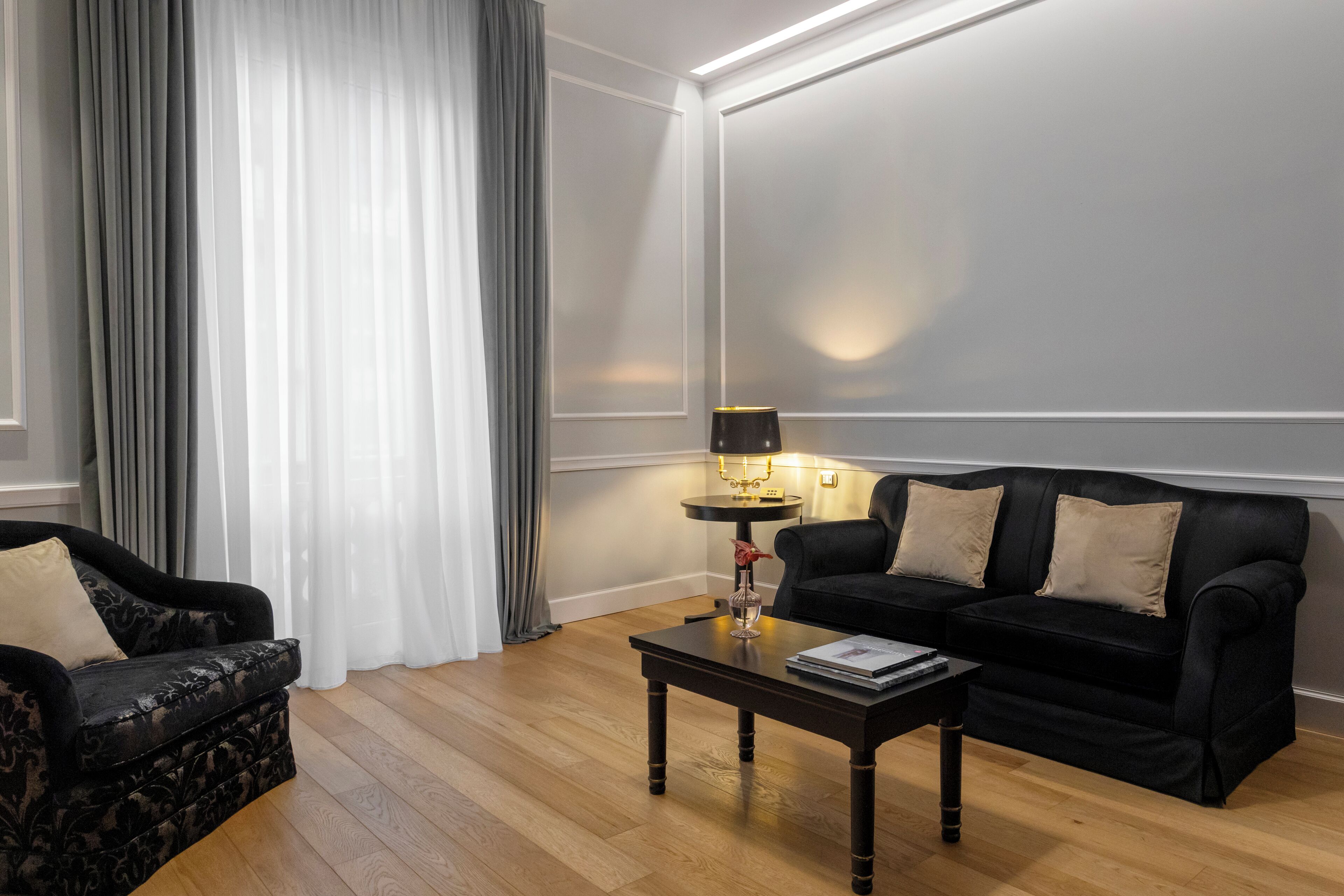 A living room with a black sofa, a patterned armchair, a wooden coffee table, and a lamp.