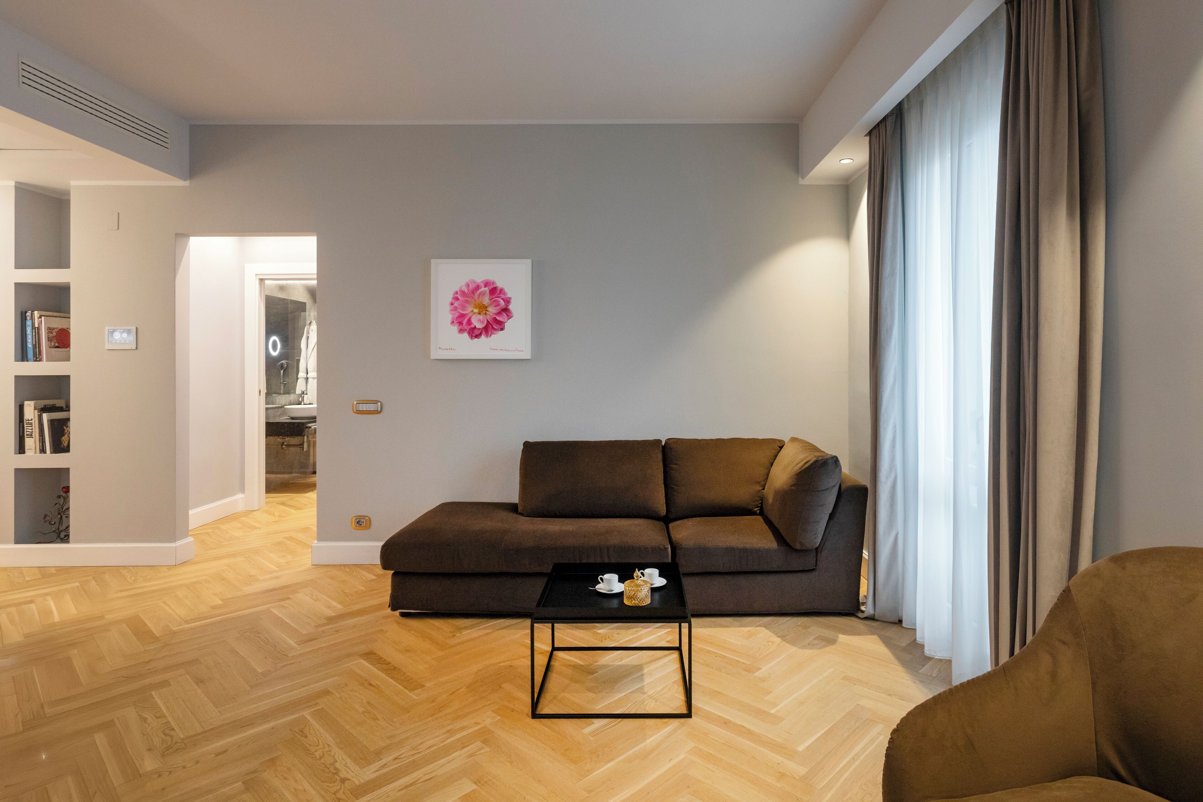 Un salon moderne avec un canapé marron, une table basse noire et un parquet en bois disposé en motif chevrons.