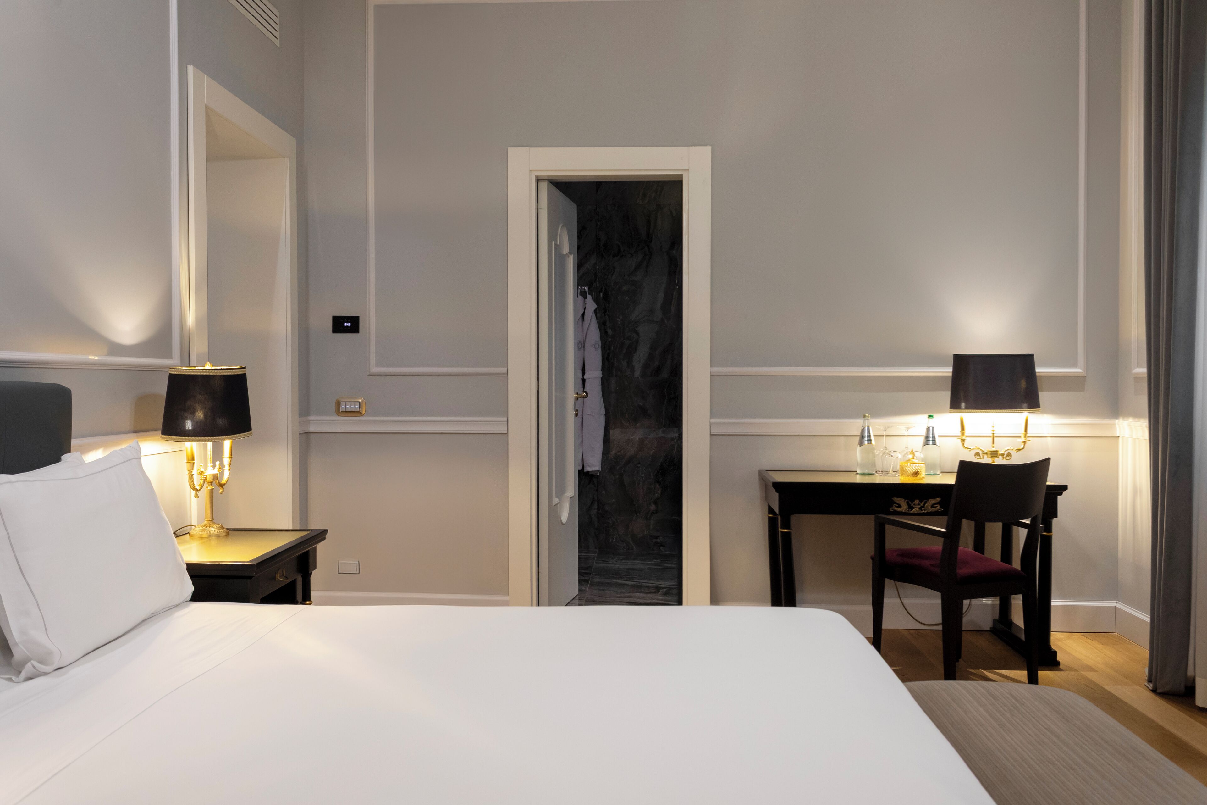 Habitación de hotel con una cama grande, dos mesitas de noche con lámparas, un escritorio con silla y un espejo en la pared.
