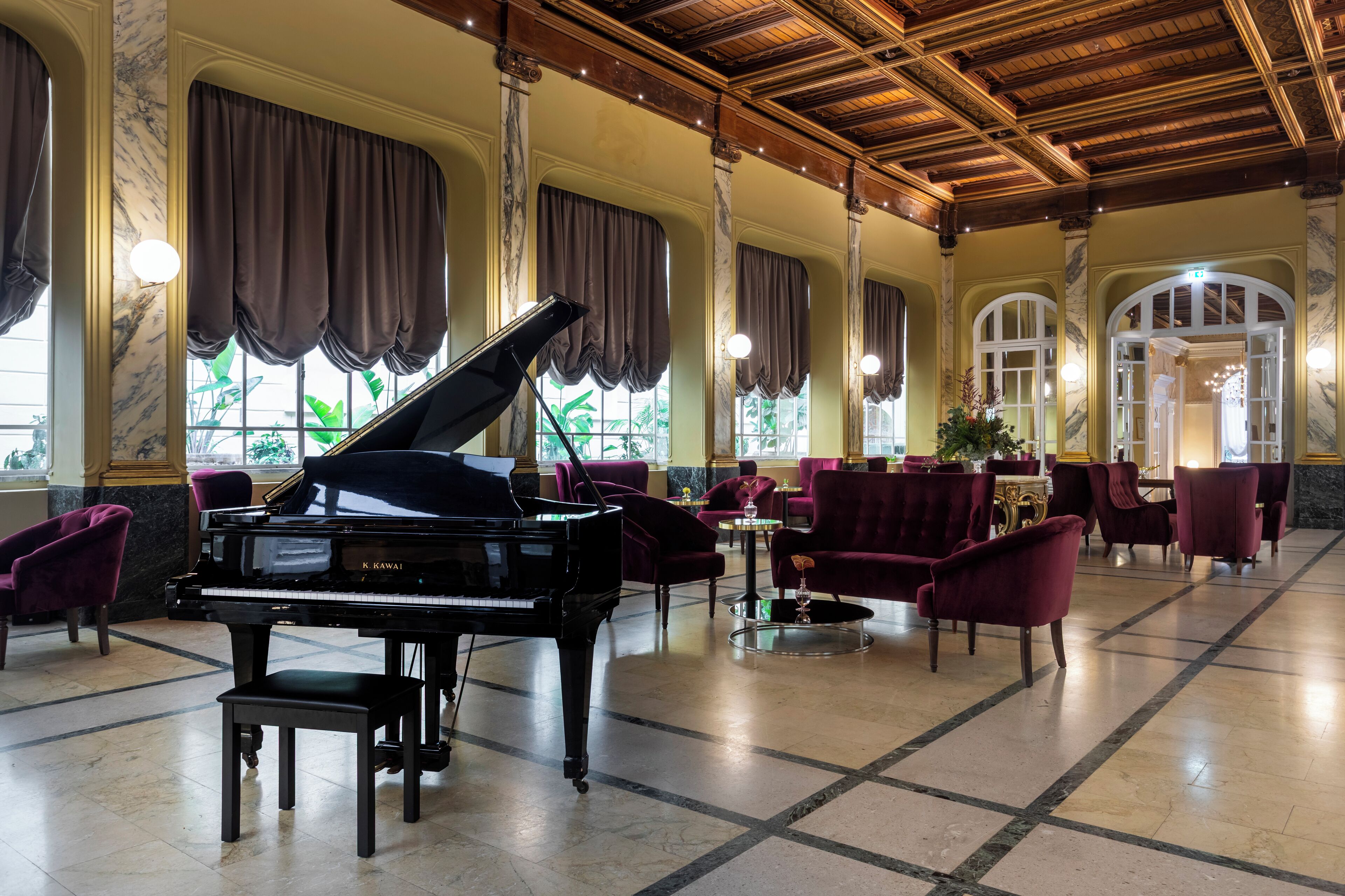 Un vaste hall d’entrée agrémenté d’un magnifique piano à queue, de colonnes en marbre et d’élégantes chaises rouges.