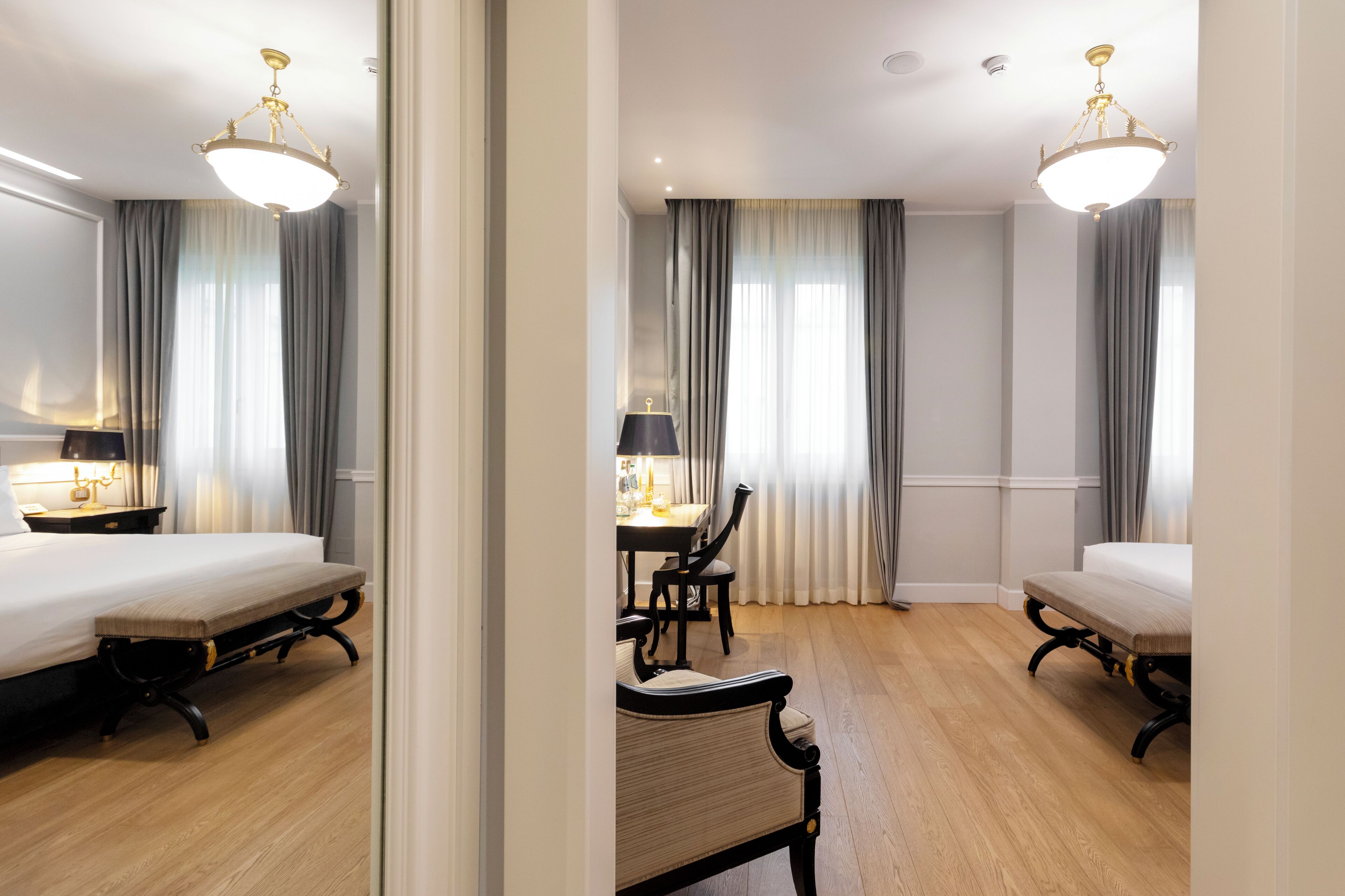 A hotel room with a bed, a desk, a chair, and a bench.