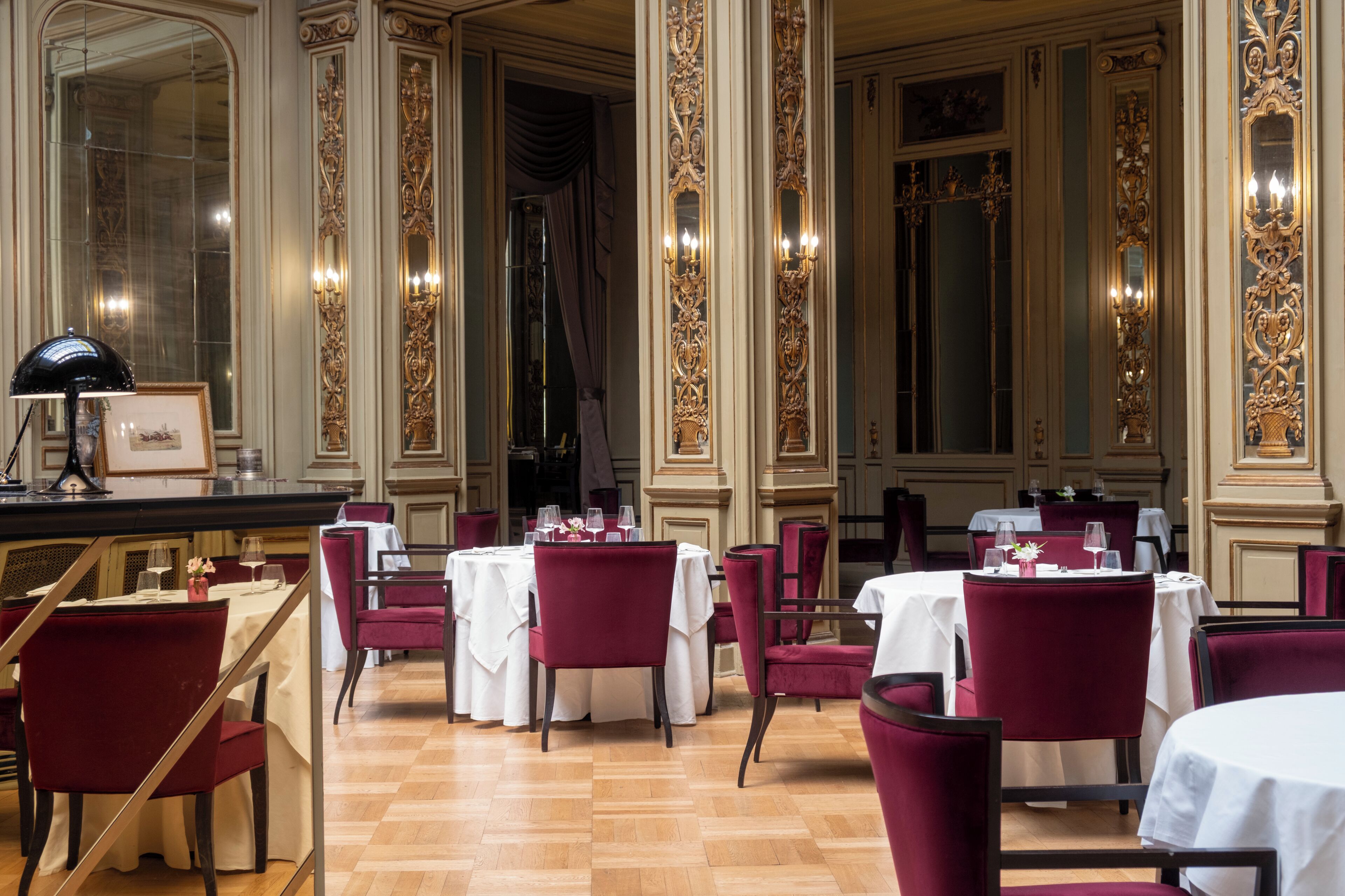 A formal dining area with tables set for four, red upholstered chairs, and ornate wall decorations.