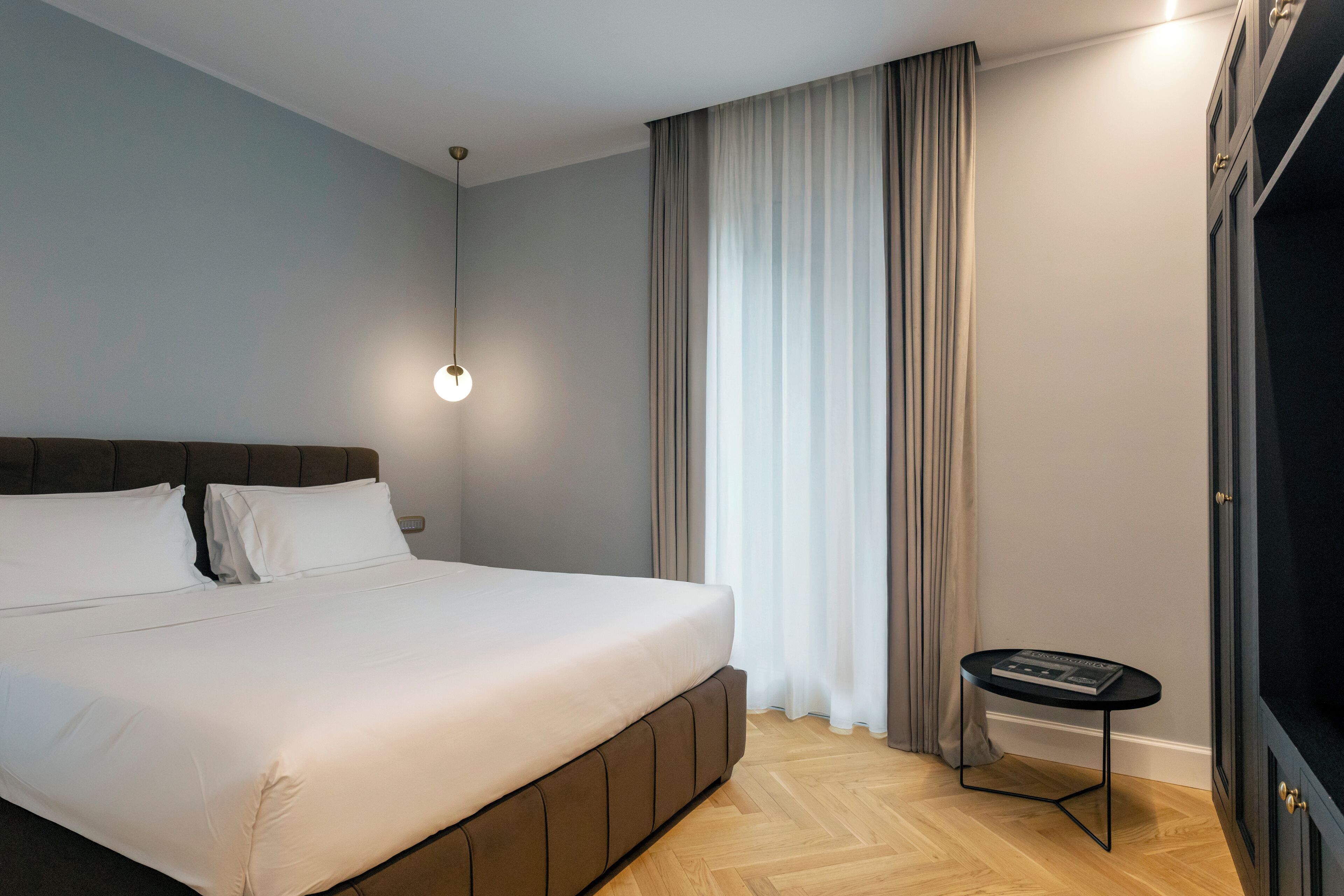 A modern hotel room with a large bed, a small side table, and a wardrobe.