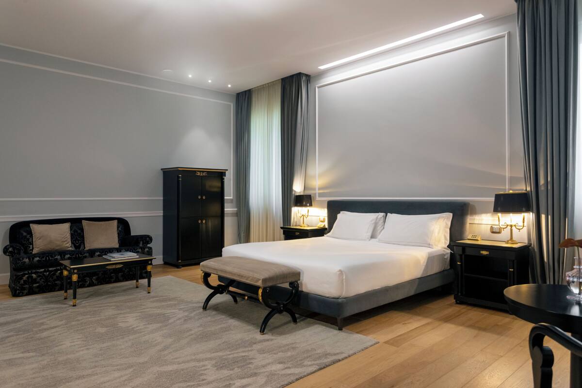 A modern hotel room with a large bed, a sofa, a small table, and a cabinet.