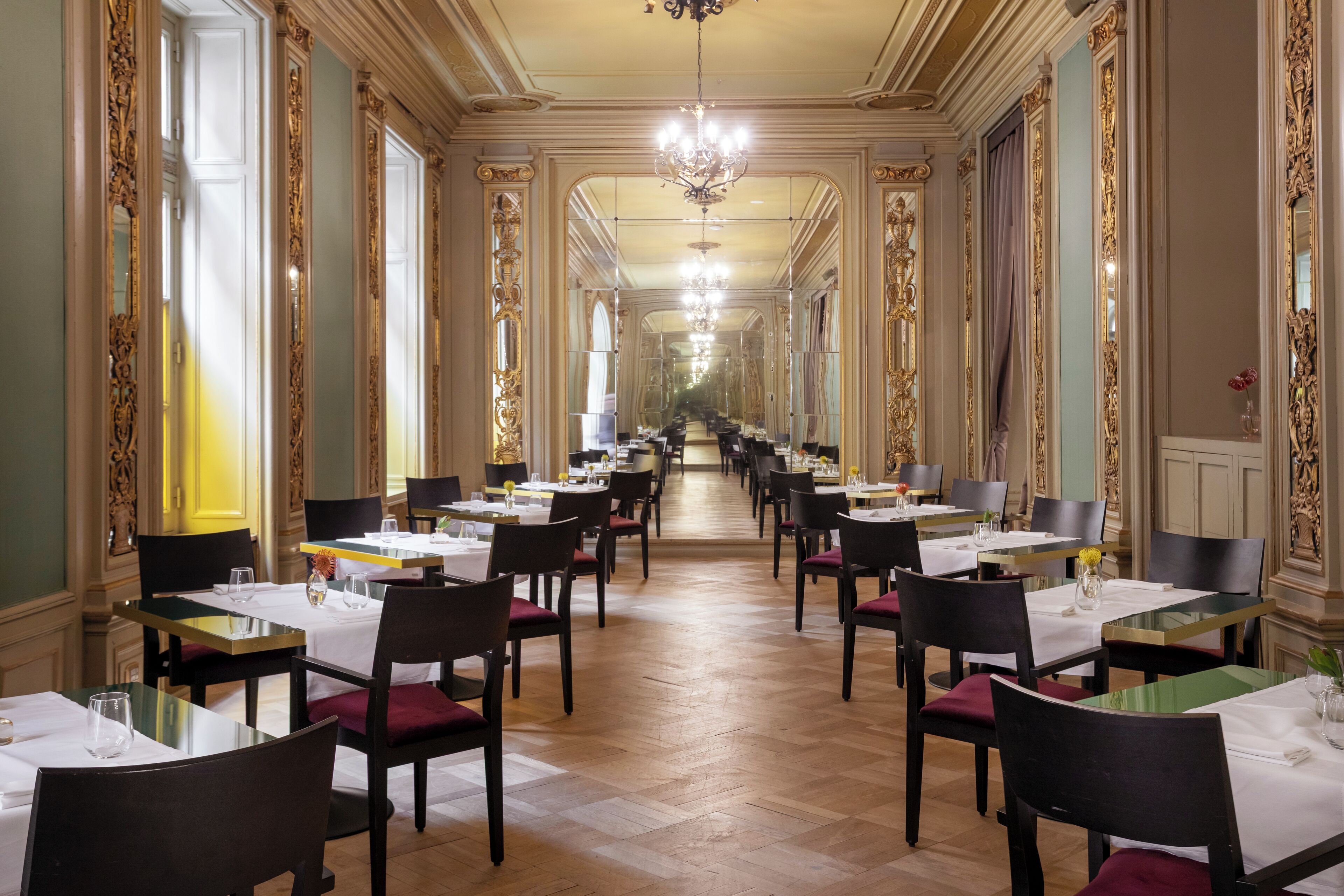 Ein langer, eleganter Speisesaal mit aufwendigen Wänden und Kronleuchtern, mit mehreren Tischen und Stühlen für das Abendessen.